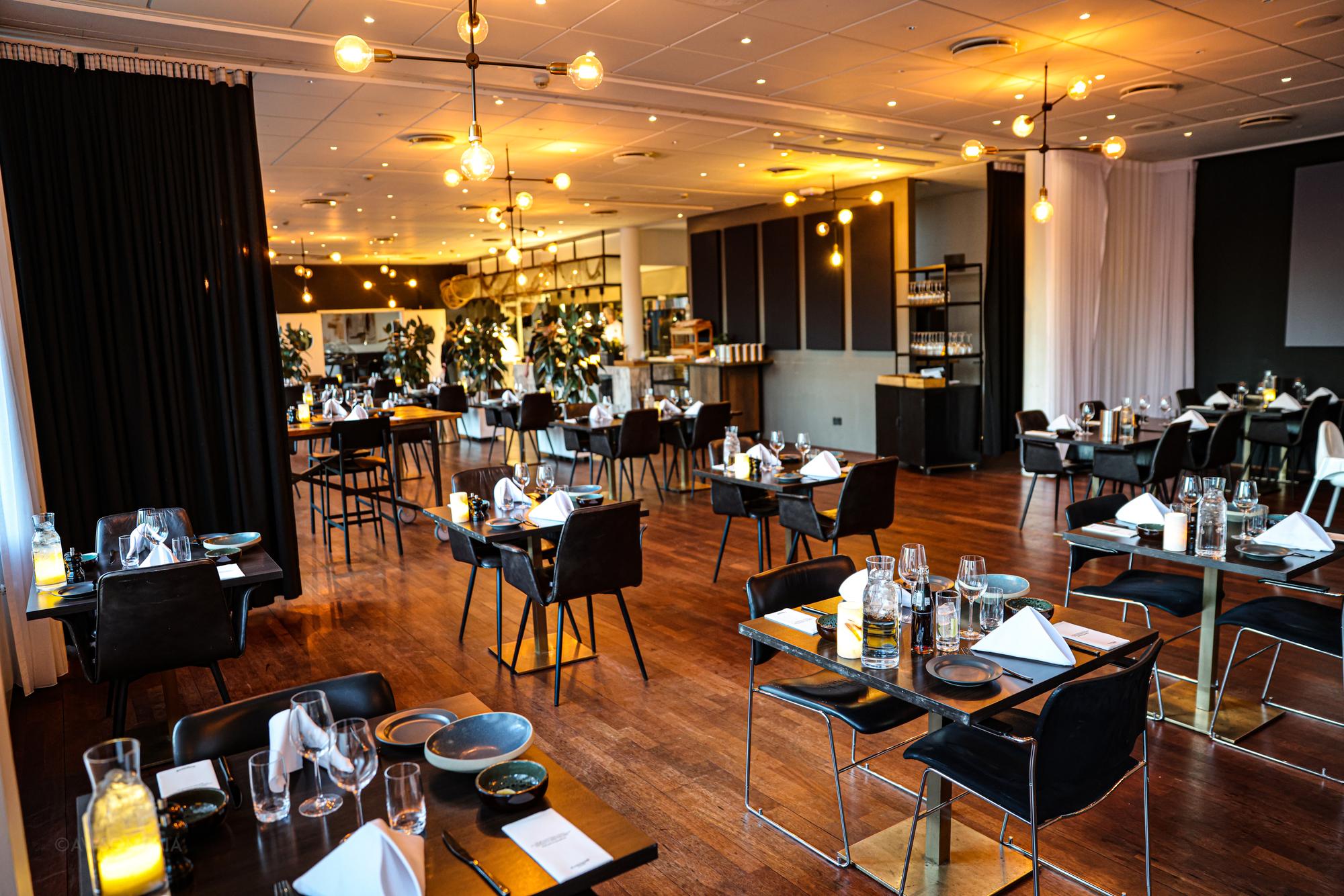 Hyggelig restaurant med træborde, stearinlys og varmt pærelys i loftet
