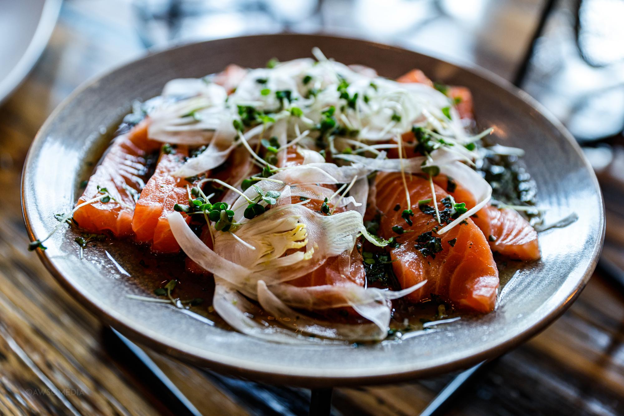 Laksecarpaccio pyntet med urter og løg på tallerken