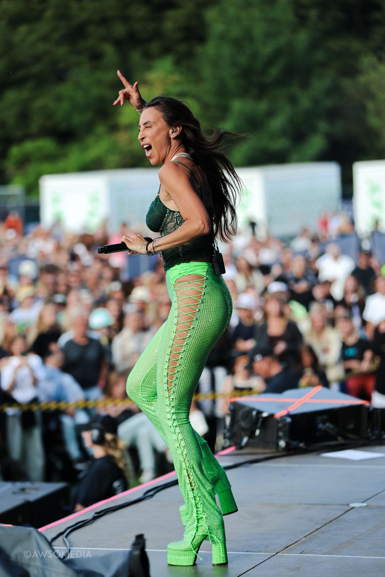 Sangerinde springer med udstrakt arm foran festivalpublikum