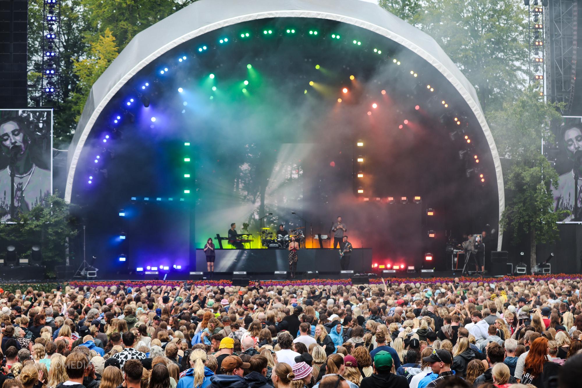 Vidtvinkelbillede af festivalscene med farvet lys og stort publikum foran
