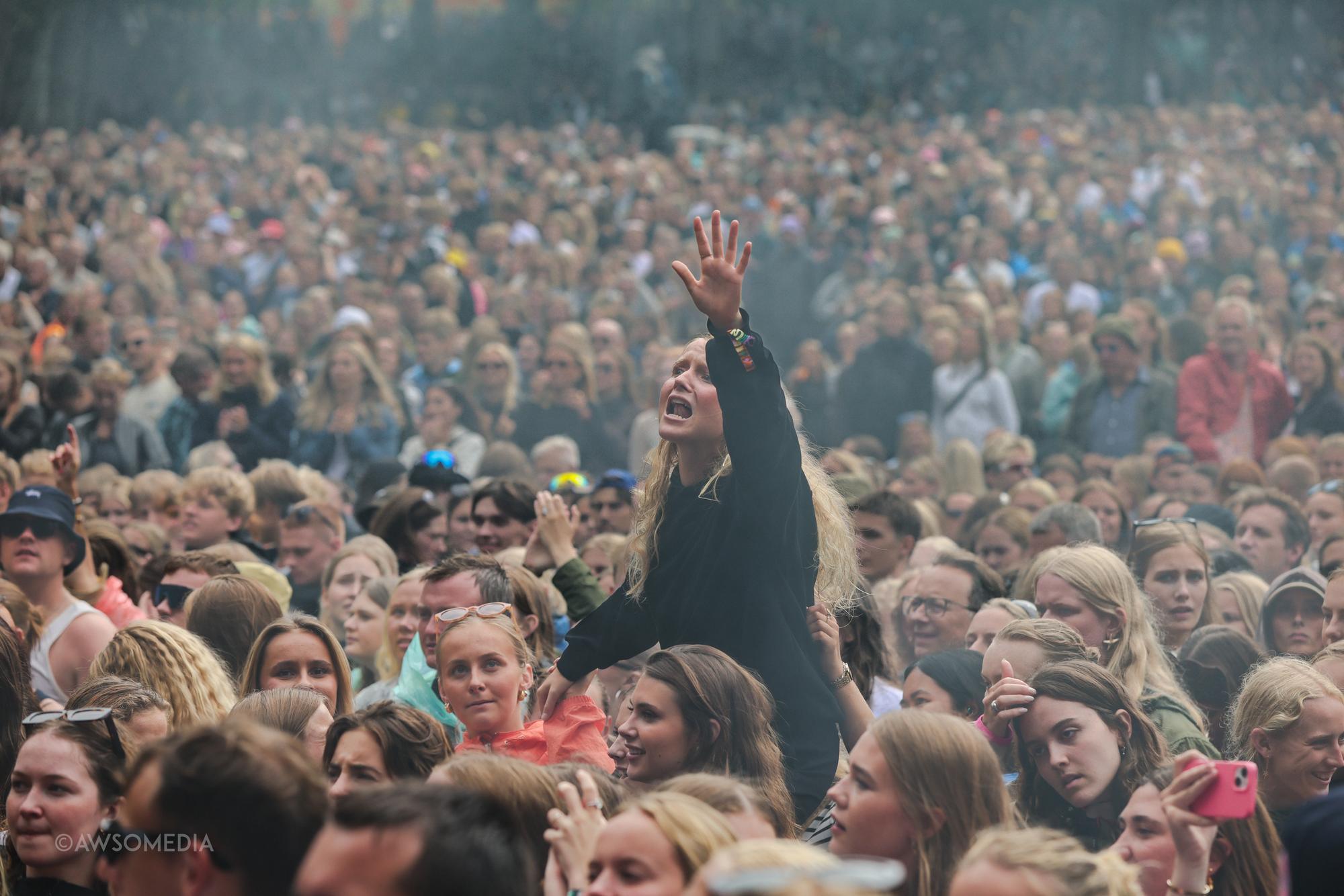 Ung kvinde rækker hånden i vejret i tæt festivalmængde med røg
