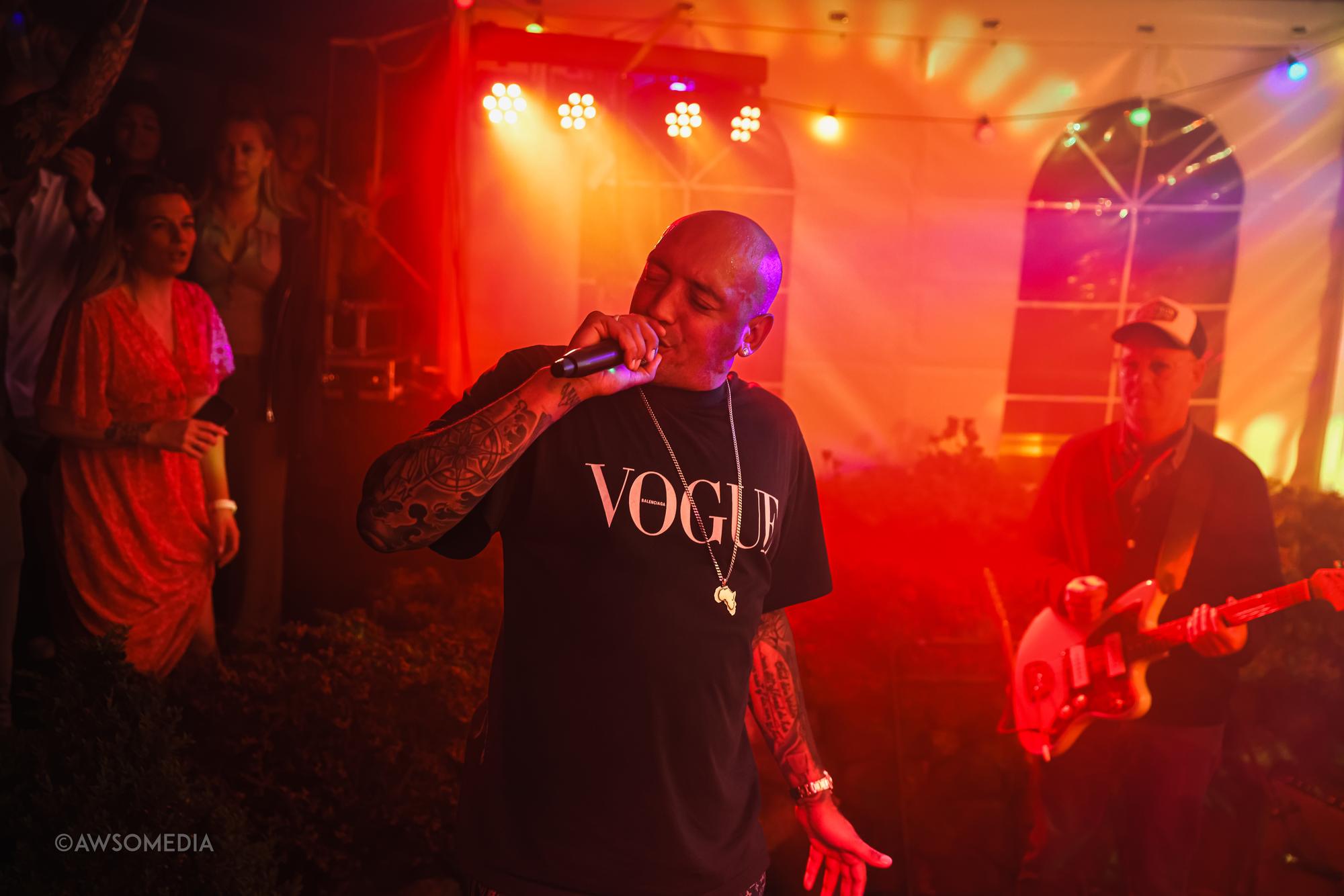 Tatoveret rapper synger i mikrofon under rødt scenelys om aftenen