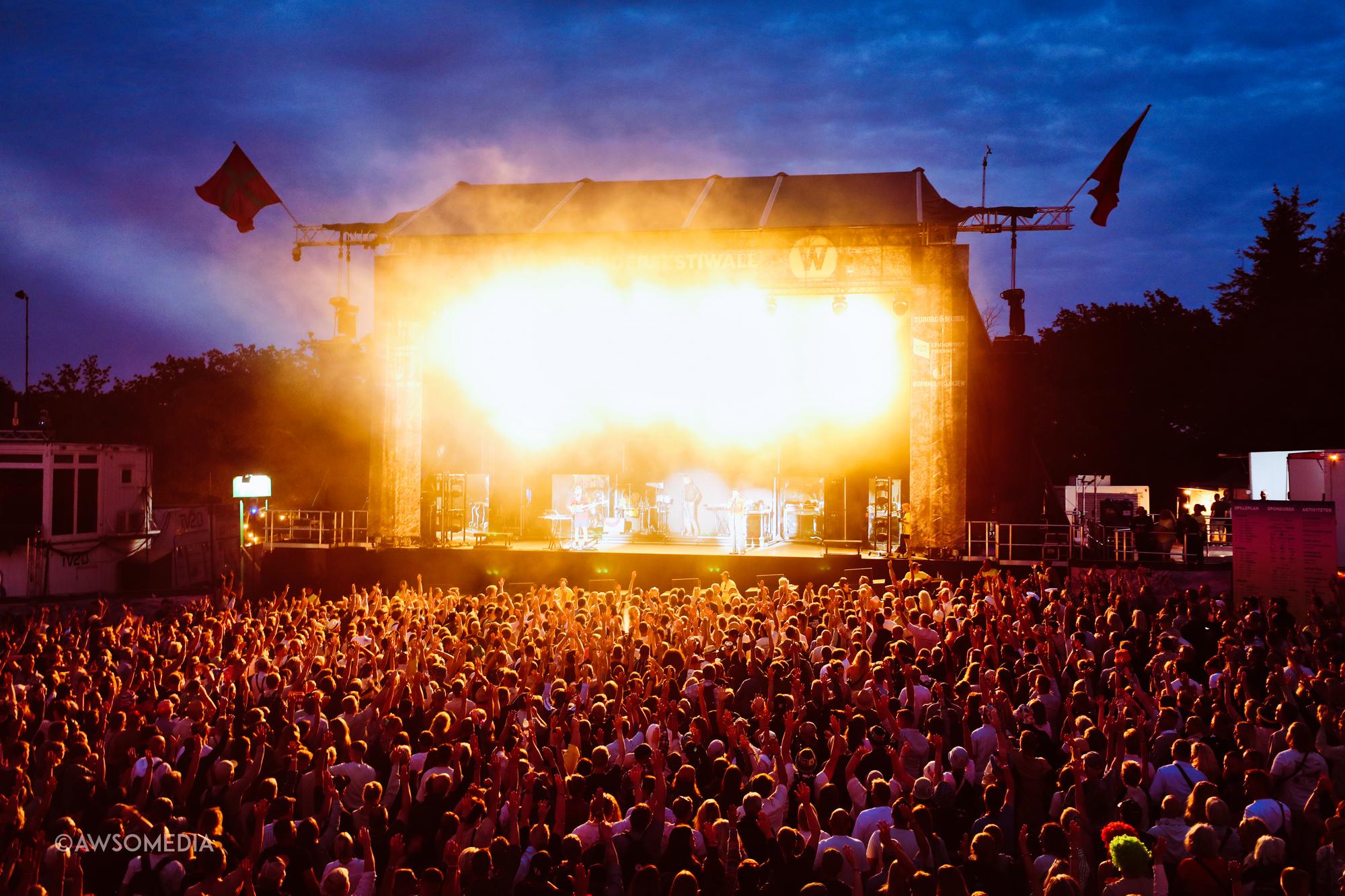 Festivalscene oplyst kraftigt med stort publikum ved solnedgang