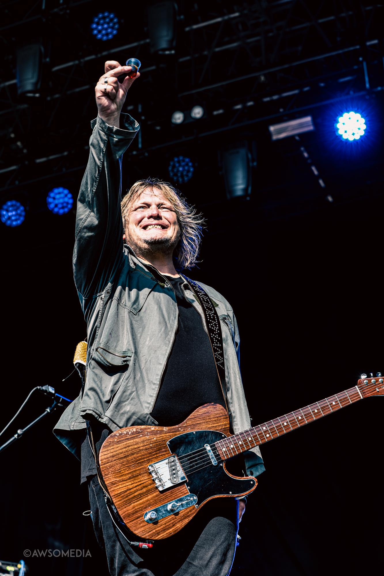 Guitarist løfter hånd triumferende foran blåt scenelys