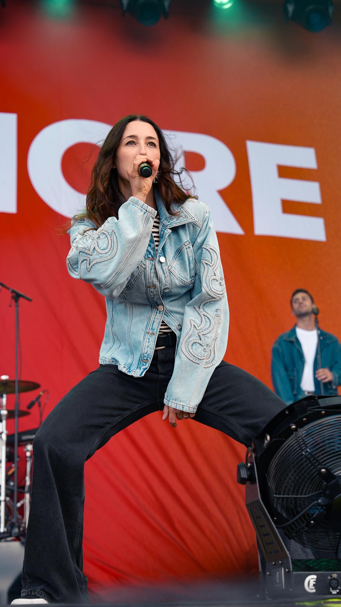 Kvinde i denimjakke poserer med mikrofon på orange festivalscene