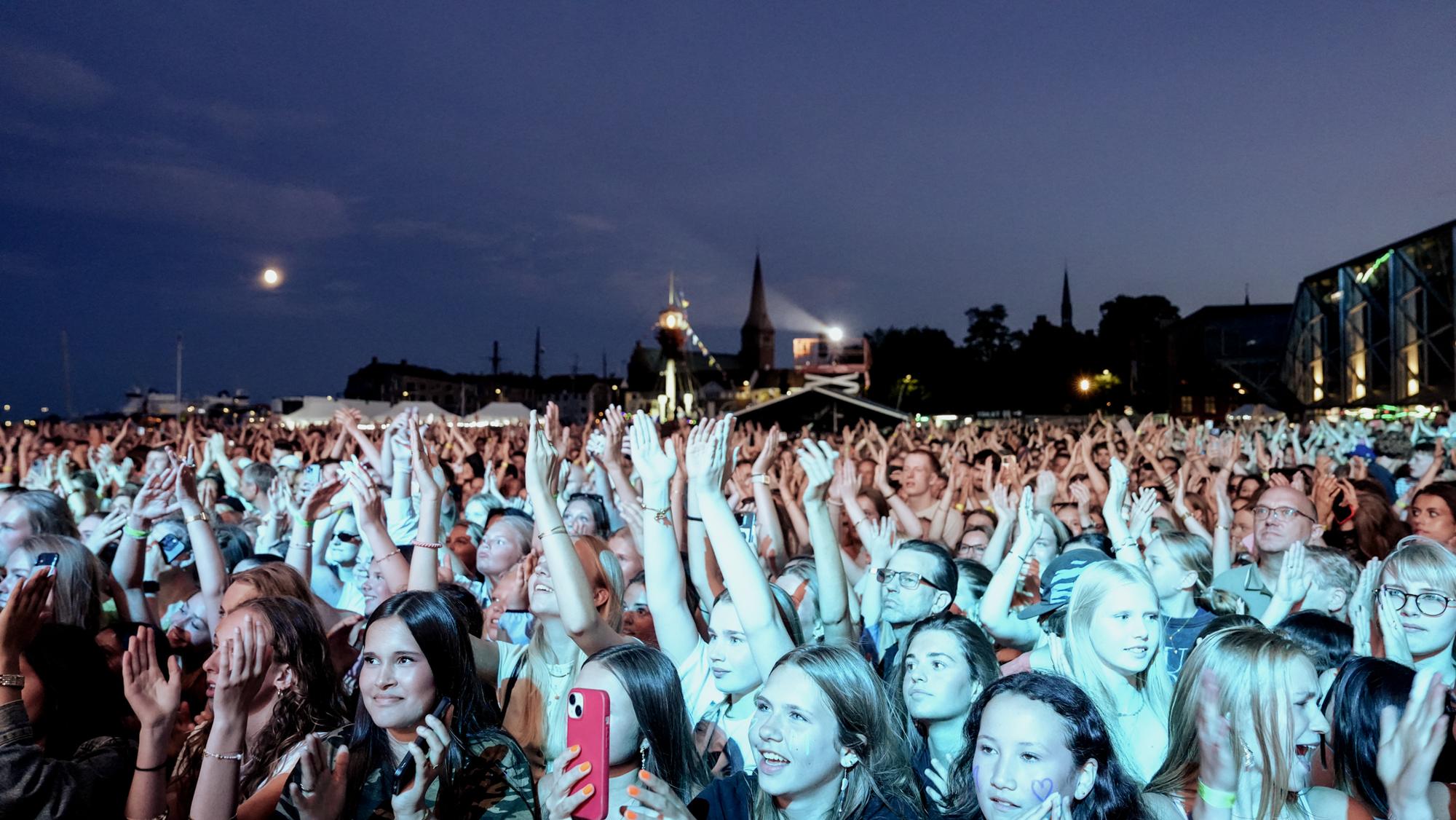 Publikum jubler med løftede arme i skumringslys ved koncert