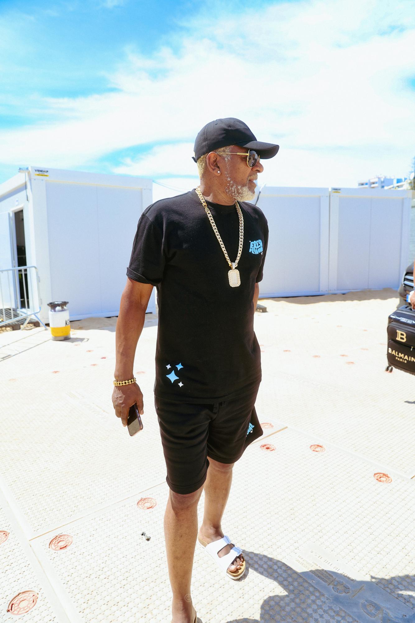Mand i sort tøj og cap går backstage i solskin