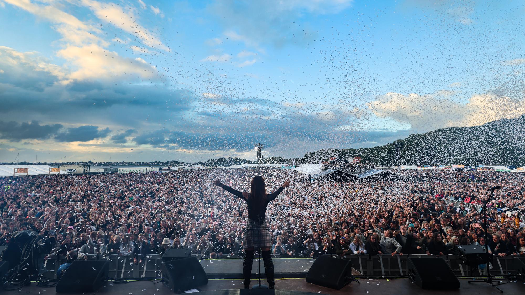 Silhuet med armene ude mens konfetti flyver over et kæmpe festivalpublikum