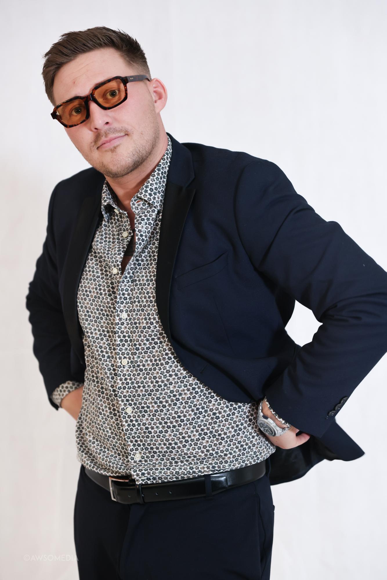 Mand med solbriller og blazer poserer foran lys baggrund