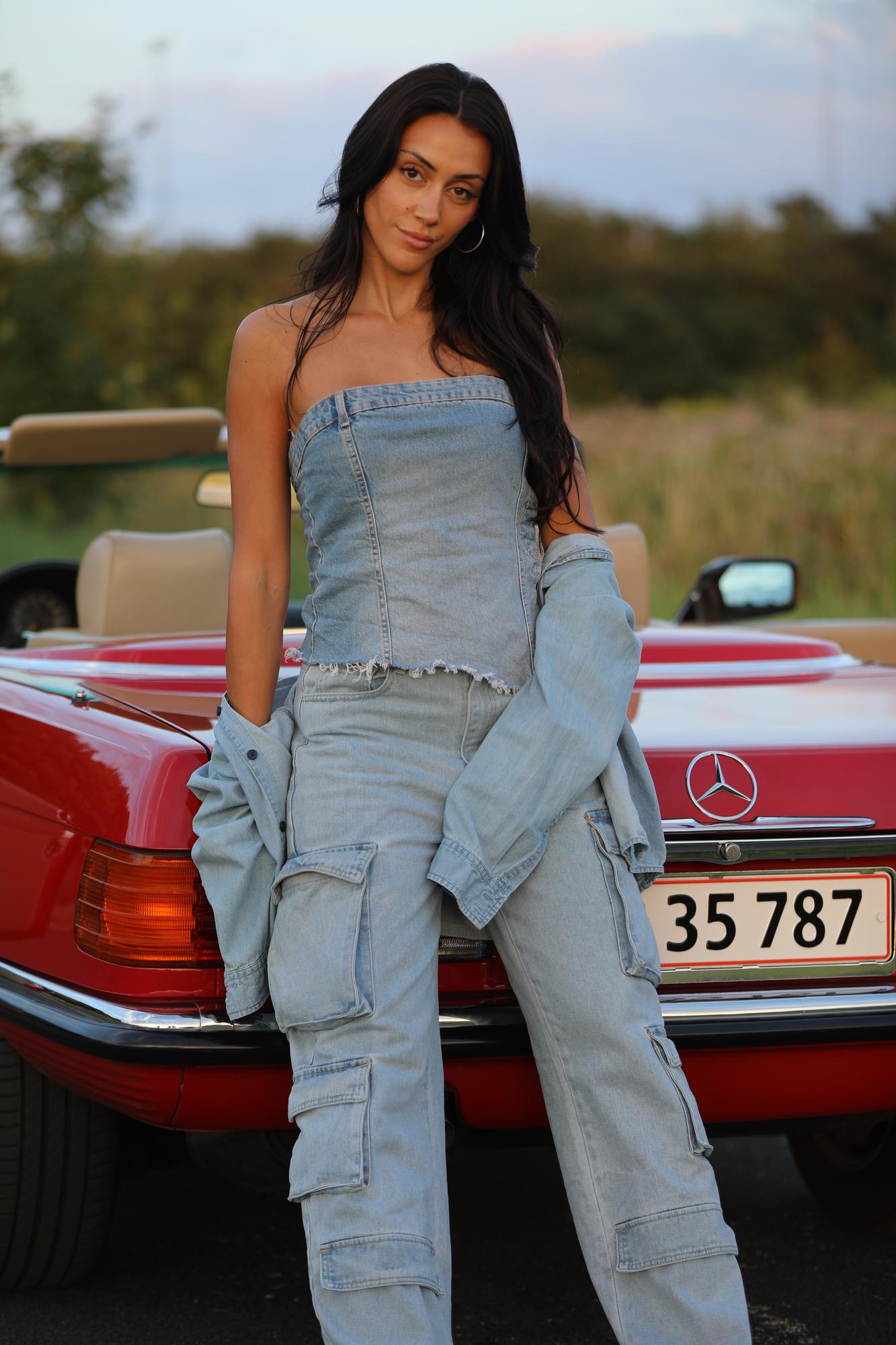 Kvinde poserer foran rød cabriolet i denim-outfit